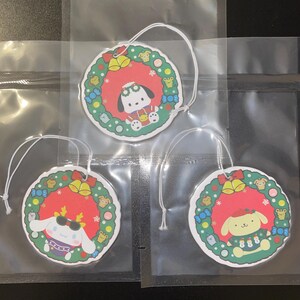 May include: Three circular Christmas decorations featuring cartoon characters within festive wreaths. Each has a white hanging string. The wreaths are red, green, and white, with small bells and other decorative elements.