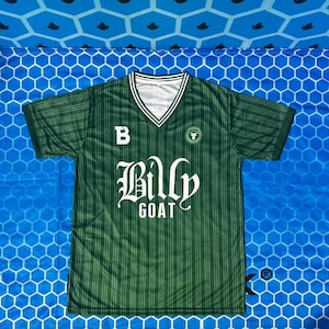 Könnte beinhalten: Grünes und weißes V-Ausschnitt-Trikot mit dem Text "Billy Goat" in gotischer Schrift. Das Trikot hat ein Streifenmuster und ein kleines Logo auf der Brust. Der Buchstabe "B" befindet sich oben links auf der Brust.