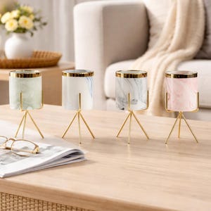 Puede incluir: Cuatro jarrones decorativos de cerámica con bordes dorados y soportes dorados con forma de trípode. Los jarrones tienen diseños de mármol en verde, blanco y rosa. Están colocados sobre una mesa de madera.