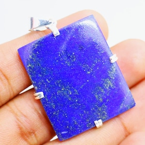 May include: A rectangular, deep blue pendant with a silver bail and four silver prongs. The pendant has a polished surface with flecks of lighter blue and green. The gemstone is held in place by silver prongs.