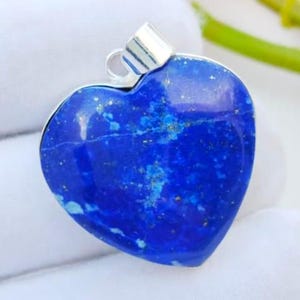 May include: A heart-shaped pendant made of deep blue lapis lazuli stone. The stone has gold flecks and a silver bail. The pendant is set against a white background.