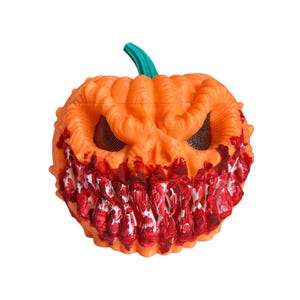May include: An orange Halloween mask shaped like a carved pumpkin with a green stem. The mask has a menacing grin with white teeth and red blood-like accents. The eyes are covered with black mesh.