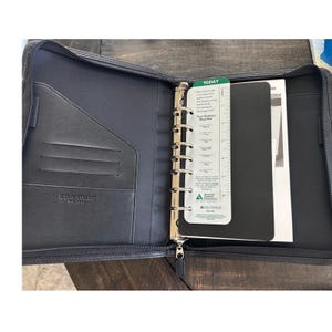 May include: A black Day-Timer zippered planner with a seven-ring metal binder mechanism. The interior features card slots and a green and white bookmark with the text Today, Your Diabetes Meal Plan, and the American Diabetes Association logo.
