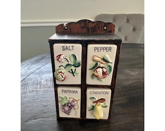 Puede incluir: Un especiero de madera marrón oscuro con cuatro cajones de cerámica blanca. Cada cajón presenta una ilustración pintada de frutas o verduras y una etiqueta: Salt con una fresa, Pepper con un higo, Paprika con uvas y Cinnamon con una pera.
