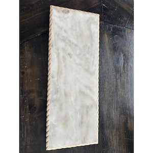 May include: A rectangular tray featuring a smooth, off-white marble surface with subtle grey veining. The tray is framed by a decorative, light-coloured rope-style border that runs along all four edges, providing a textured contrast to the stone.