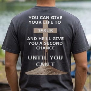 Puede incluir: Una camiseta gris oscuro con el texto "YOU CAN GIVE YOUR LIFE TO JESUS AND HE'LL GIVE YOU A SECOND CHANCE UNTIL YOU CAN'T" impreso en la espalda. La camiseta se lleva al aire libre cerca de un lago.