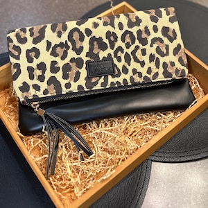 May include: A black and tan leopard print clutch with a black leather bottom. The clutch is in a wooden box with shredded paper. The text "FUNKY MONKEY" is on a black label on the front of the clutch.