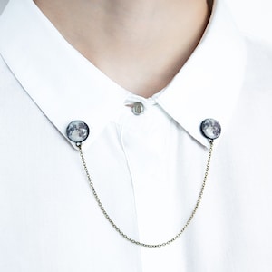 May include: A silver chain collar clip with a moon image on each end. The chain is attached to a white collared shirt.
