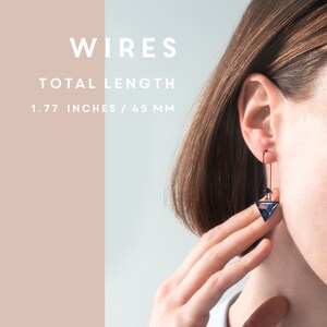 Puede incluir: Un par de pendientes con un dise&ntilde;o de tri&aacute;ngulo geom&eacute;trico. Los pendientes est&aacute;n hechos de alambre negro y tienen un colgante de vidrio triangular azul y rosa. Los pendientes miden 4,5 cm de largo.