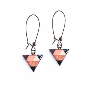 May include: A pair of triangle-shaped earrings with a geometric pattern in shades of pink, black, and brown. The earrings are suspended from gold-toned hooks.
