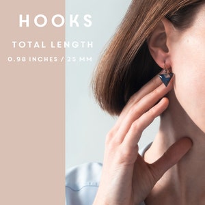 Puede incluir: Un par de pendientes con un colgante en forma de tri&aacute;ngulo. Los pendientes est&aacute;n hechos de resina azul oscuro y negra y tienen un gancho plateado. Los pendientes miden 2,5 cm de largo.
