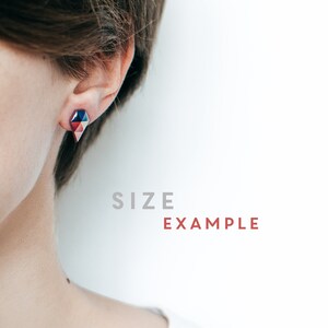 May include: Geometric stud earrings in shades of red, blue, and pink. The earrings have a faceted design and are worn on the ear. The text "SIZE EXAMPLE" is visible in the background.