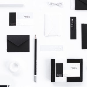 May include: A flat lay image of a minimalist jewelry brand's packaging and branding materials. The image features a black and white color scheme with a variety of items, including a small box, envelopes, business cards, and a pencil. The business cards feature the brand name "LEPUN" and the tagline "MINIMALIST JEWELRY".