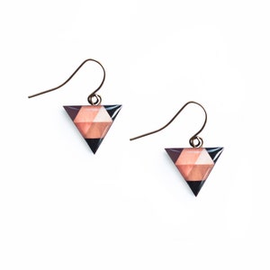 May include: A pair of triangle-shaped earrings with a geometric pattern in shades of pink, brown, and black. The earrings have a simple gold hook closure.
