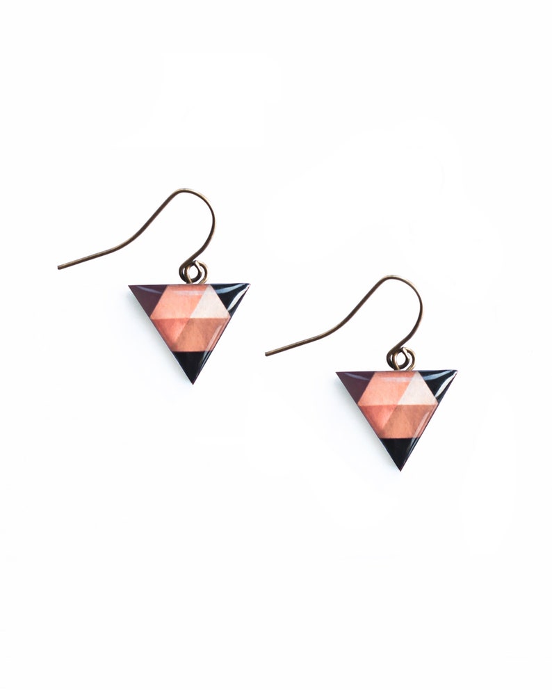 May include: A pair of triangle-shaped earrings with a geometric pattern in shades of pink, brown, and black. The earrings have a simple gold hook closure.