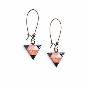 May include: A pair of triangle-shaped earrings with a geometric pattern in shades of brown, pink, and black. The earrings are made of metal and have a hook closure.