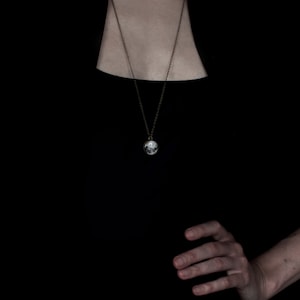 May include: A silver pendant necklace with a round charm depicting a detailed moon. The necklace has a delicate chain and is displayed against a black background. The charm is approximately 0.75 inches in diameter.