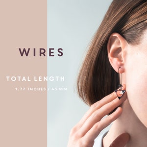 May include: Wires earrings with a geometric triangle design in shades of black, pink, and white. The earrings are 1.77 inches / 45 mm long.