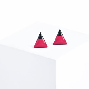 Peut inclure: Une paire de boucles d'oreilles triangulaires. Chaque boucle d'oreille est divisée en deux sections : une base rose-rouge vibrante et un sommet noir brillant. Les boucles d'oreilles sont présentées sur une surface blanche, créant une esthétique épurée et moderne.