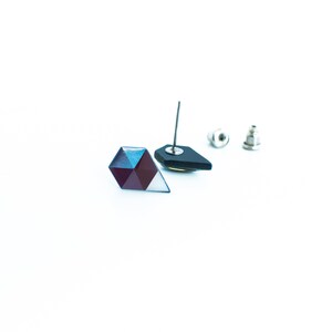 May include: Geometric stud earrings with a faceted, multi-colored design. One earring is a dark, angular shape with a silver post. The other earring is a multi-faceted shape with shades of blue, purple, and white. The earring backs are also visible.