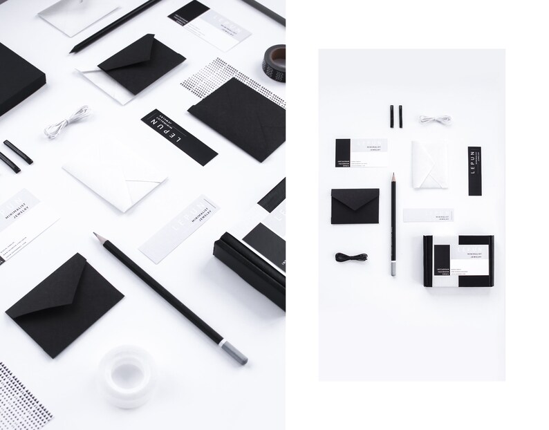 May include: An overhead shot of stationery items in black and white. The items include envelopes, pencils, business cards, a small box, and a roll of tape. The text "LEPUN" and "MINIMALIST JEWELRY" are visible on some of the items.