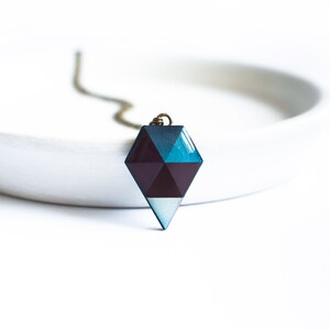 Op de afbeelding: Een geometrische, diamantvormige hangerketting met een blauw, paars en wit kleurenschema. De hanger is gemaakt van hars en heeft een glanzende afwerking.
