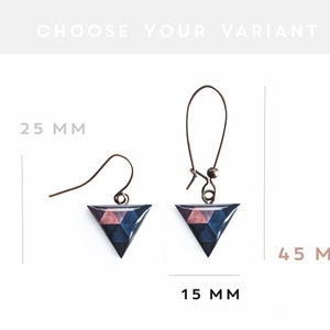 Puede incluir: Un par de pendientes triangulares geom&eacute;tricos con un patr&oacute;n rosa, azul y negro. Los pendientes miden 4,5 cm de alto y 1,5 cm de ancho. Los pendientes est&aacute;n hechos con un gancho plateado.