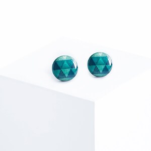 May include: Two round stud earrings with a geometric triangle pattern in shades of teal and green. The earrings are set against a white background, highlighting their design and color.