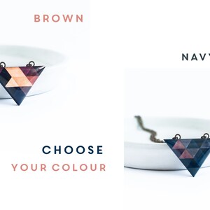 May include: Geometric triangle pendant necklace in brown and navy blue color options. The pendant features a mosaic design with various shades of brown, pink, and navy blue. The necklace is displayed on a white dish.