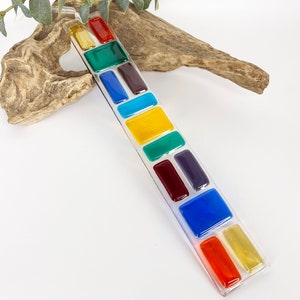 May include: A long, clear glass panel with a series of colourful rectangular glass tiles embedded in it. The tiles are arranged in a vertical line and feature shades of red, orange, yellow, green, blue, and purple.