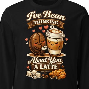 May include: Black long-sleeve shirt with a coffee-themed graphic. The design features a smiling coffee bean hugging a smiling coffee cup, with the text "I've Bean Thinking About You A Latte". Includes hearts, sugar cubes, and a croissant.