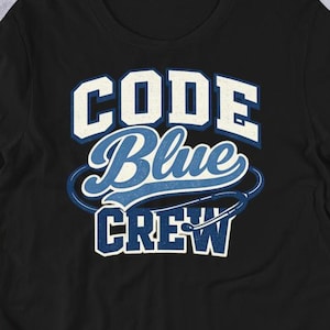 Puede incluir: Camiseta negra con el texto "CODE Blue CREW" en letras blancas y azules. El diseño tiene una estética de colegio o equipo deportivo. La camiseta está hecha de un material suave y es adecuada para ropa casual. El diseño está en una fuente clara y en negrita.