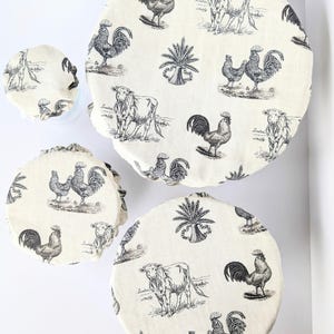 May include: A set of reusable bowl covers in various sizes. The covers feature a cream-colored background with a black toile pattern of roosters, cows, and palm trees. The covers are arranged on a white surface.