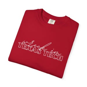 May include: A red t-shirt with the phrase "wreck 'em TEXAS TECH" in white script and block letters. The shirt is folded and has a tag in the upper right corner.