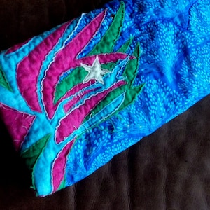 May include: A blue, pink, and green quilted fabric with a white star in the center. The fabric has a floral design.
