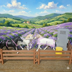 May include: A toy horse set featuring three miniature horses in a scenic landscape. One black horse, one white horse, and one tan horse with a blanket. The background shows a lavender field, rolling hills, and a blue sky.