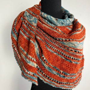 May include: A knitted shawl with a rust and blue color scheme. The shawl is made with a delicate stitch pattern and has a fringed edge.