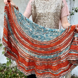 May include: A teal and orange knitted shawl with a scalloped edge. The shawl has a repeating pattern of stripes and lace.