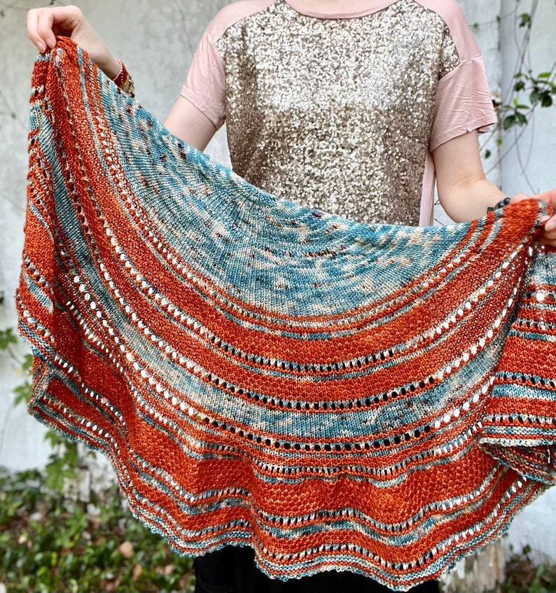 May include: A teal and orange knitted shawl with a scalloped edge. The shawl has a repeating pattern of stripes and lace.