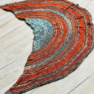 May include: A hand-knitted shawl in shades of blue and orange with a circular pattern. The shawl is made with a soft yarn and has a delicate texture.
