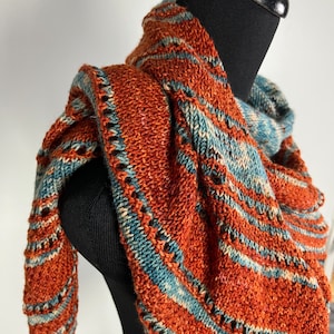 May include: A knitted shawl with a triangular shape, featuring a rust orange and teal blue color scheme. The shawl is made with a textured stitch and has a fringe border.