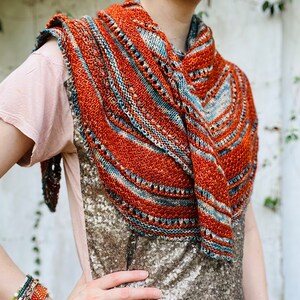 May include: A knitted shawl with a rust, blue, and cream color pattern. The shawl is draped over a person's shoulders.