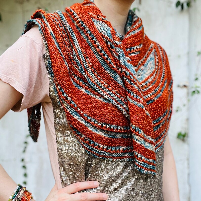 May include: A knitted shawl with a rust, blue, and cream color pattern. The shawl is draped over a person's shoulders.