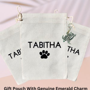May include: Three white cotton drawstring pouches with black paw print and the name "Tabitha" printed on them. One pouch has a silver turtle charm attached.