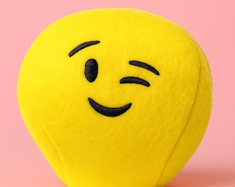 May include: A plush, yellow emoji with a winking eye and a smiling mouth. The emoji is a soft, round shape, perfect for a child's toy or a decorative item. The facial features are embroidered in black.