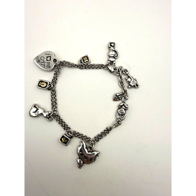 Pode incluir: Pulseira de berloques prateada com berloques com tema de gato. A pulseira inclui um berloque em forma de cora&ccedil;&atilde;o com o texto "I my CAT", silhuetas de gatos, espinhas de peixe e berloques de tigelas de comida. Fundo branco.