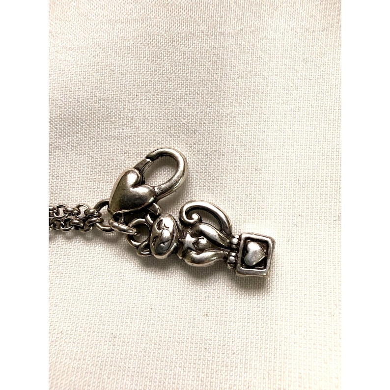 Pode incluir: Close-up de um fecho de colar prateado com elementos de cora&ccedil;&atilde;o e decorativos. O fecho apresenta um fecho em forma de cora&ccedil;&atilde;o e um berloque com um design em forma de cora&ccedil;&atilde;o. A corrente do colar &eacute; vis&iacute;vel.