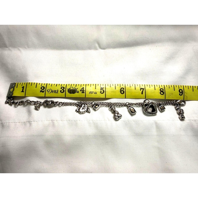 Pode incluir: Uma pulseira de prata com v&aacute;rios berloques, incluindo cora&ccedil;&otilde;es, um rel&oacute;gio, uma fechadura e um cadeado. A pulseira tem aproximadamente 20 cm de comprimento, medida com uma fita m&eacute;trica amarela. Os berloques s&atilde;o detalhados.