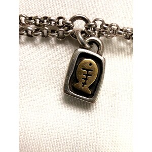 Pode incluir: Colar prateado com um pendente retangular com um desenho de espinha de peixe dourada. O pendente &eacute; emoldurado em prata e pendurado numa corrente de dupla fileira. A joia &eacute; apresentada sobre um fundo branco.