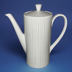 Puede incluir: Cafetera de cerámica blanca con tapa y boquilla larga. La jarra tiene un cuerpo cilíndrico con líneas verticales grises. Cuenta con un asa curva y un pequeño pomo en la tapa. El fondo es azul liso.